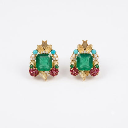 Pair of gold stud earrings with emerald-cut green centre stones, gold leaves, ruby-pink stone clusters, turquoise beads and pearls on a white background