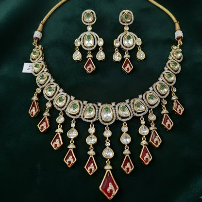 Gold-tone kundan necklace set with red kite-shaped drops, green accent stones and matching chandelier earrings on a grey display bust