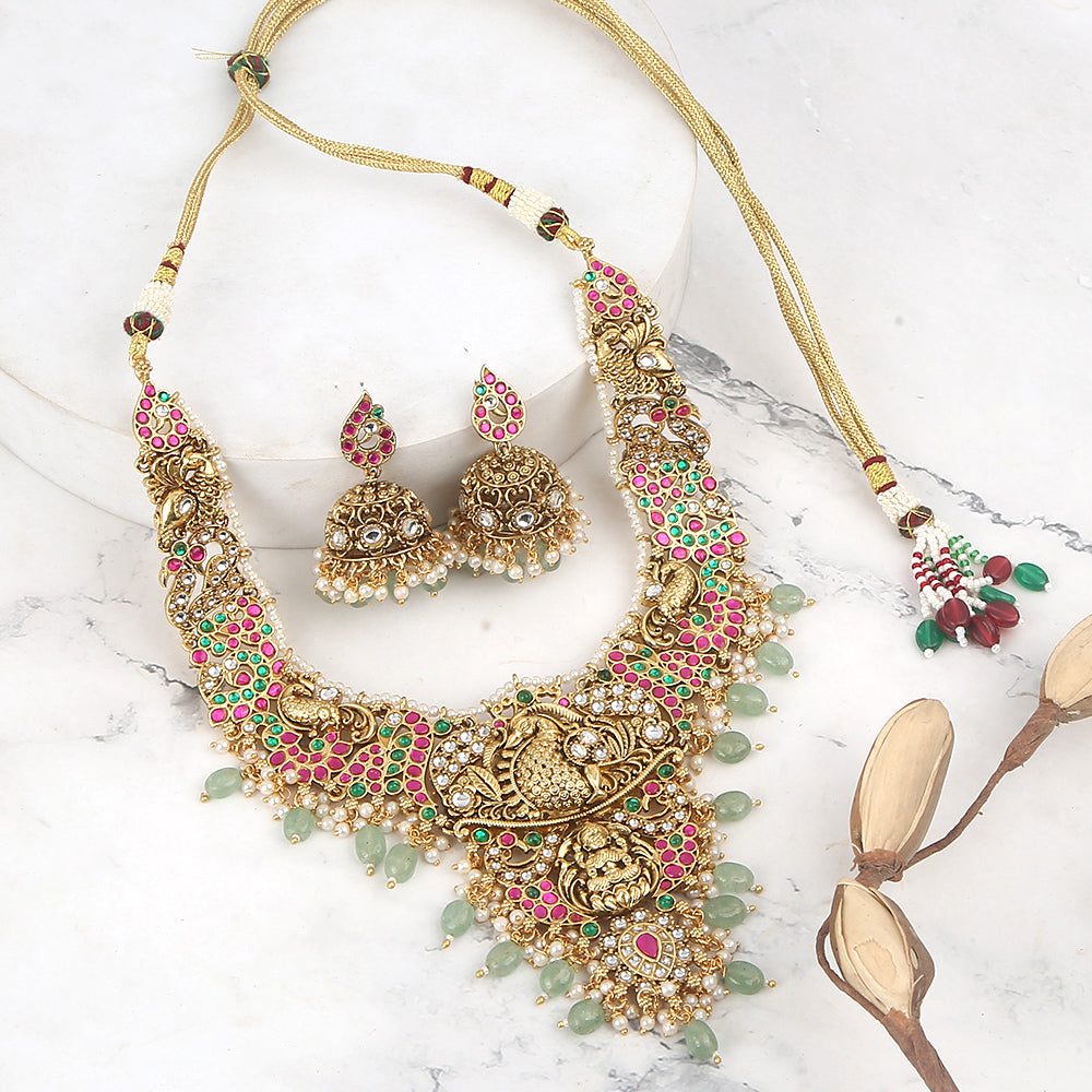Gold plated temple Lakshmi bridal necklace set with pink green stones and jhumka earrings with pearl and bead drops on white background