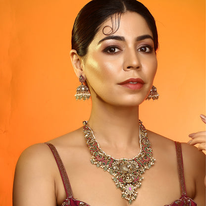 Gold plated temple Lakshmi bridal necklace set with pink green stones and jhumka earrings with pearl and bead drops on white background