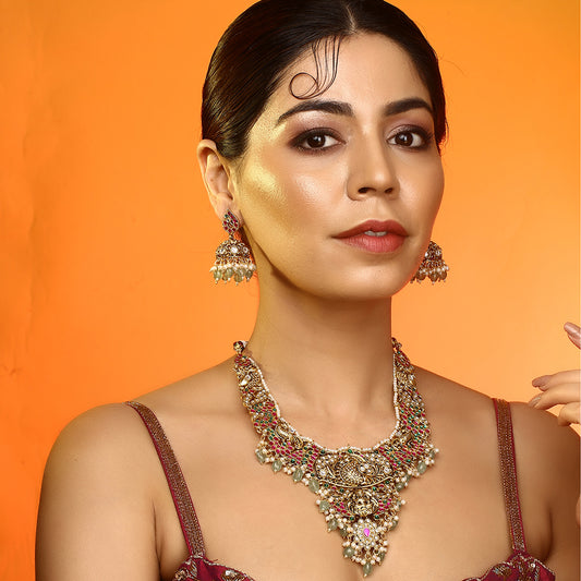 Gold plated temple Lakshmi bridal necklace set with pink green stones and jhumka earrings with pearl and bead drops on white background