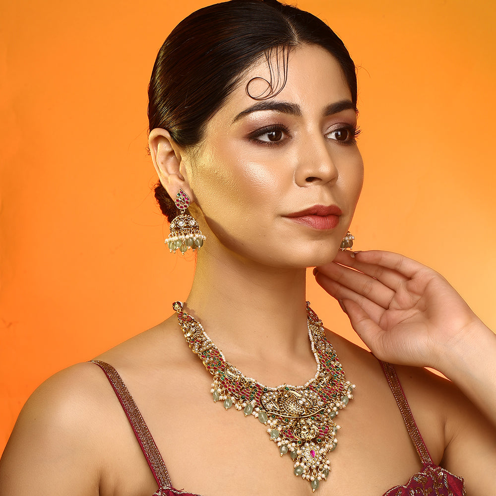 Gold plated temple Lakshmi bridal necklace set with pink green stones and jhumka earrings with pearl and bead drops on white background