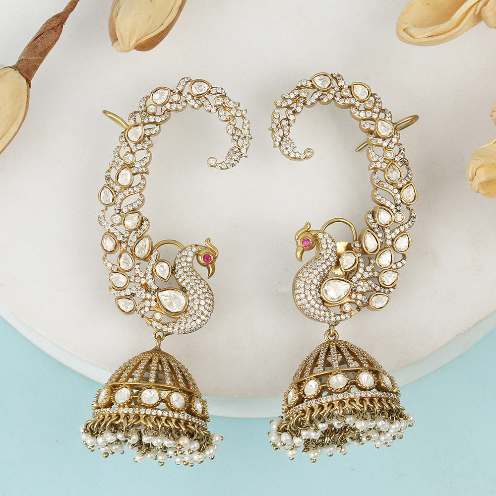 Gold plated peacock design jhumka earrings with American diamonds and pearl drops on white background