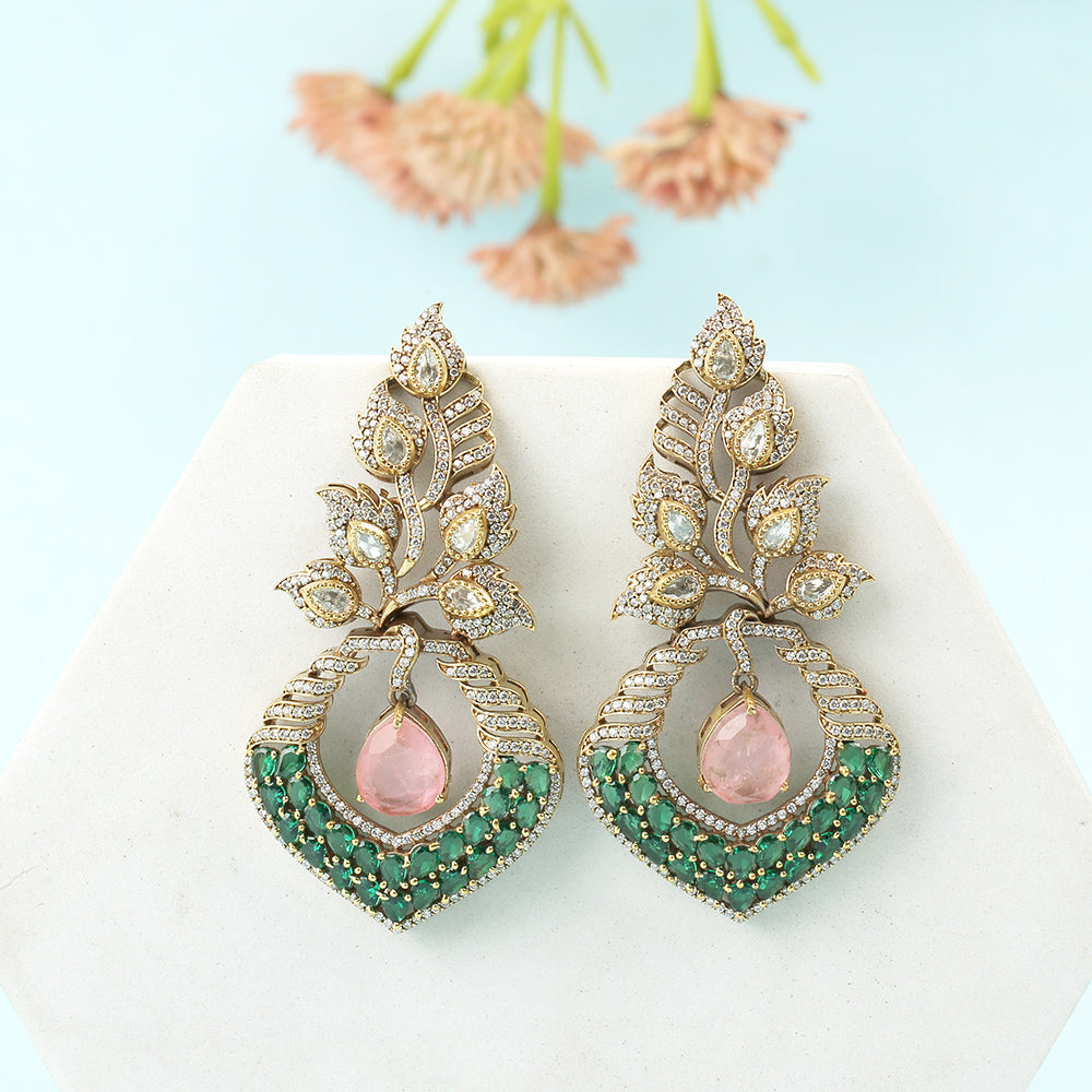 Gold plated American diamond earrings with leaf design, green stones and pink drop hanging centerpiece on white background
