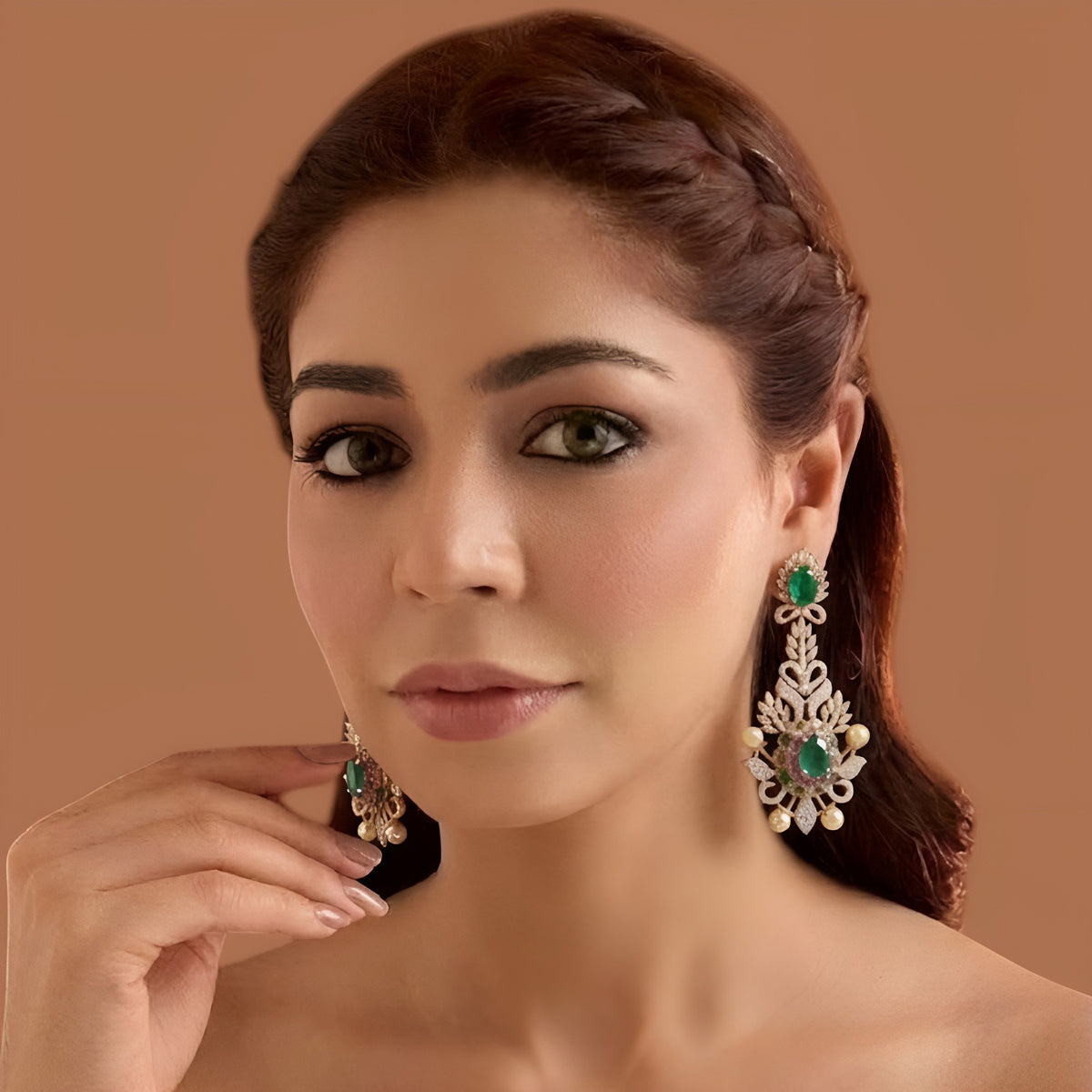 Rose gold plated emerald green American diamond long chandelier earrings with pink stones and pearl accents held in hand