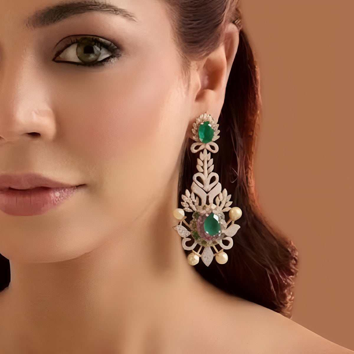 Rose gold plated emerald green American diamond long chandelier earrings with pink stones and pearl accents held in hand