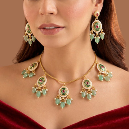 Gold plated mint green oval medallion necklace set with pink stones, green bead and pearl drops and matching earrings on a blue bust