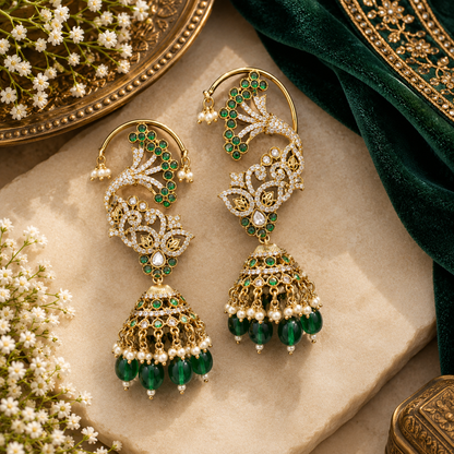 Gold plated emerald green ear cuff jhumka earrings with American diamond stones, green beads and pearl hangings on a white background