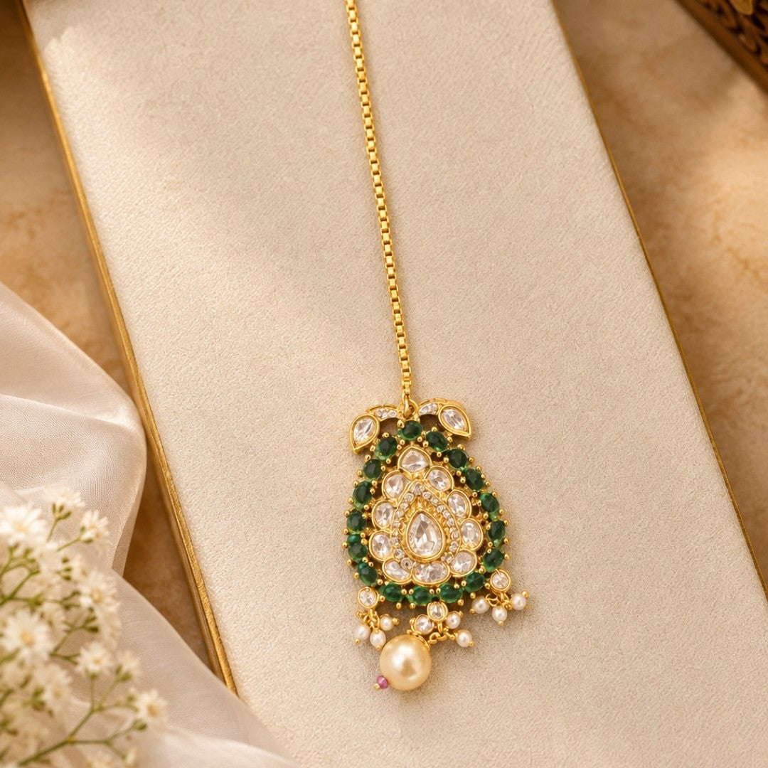 Gold-plated kundan polki paisley maang tikka with emerald green stone border, clear pear centre stone, cream pearl drop and box chain with hook