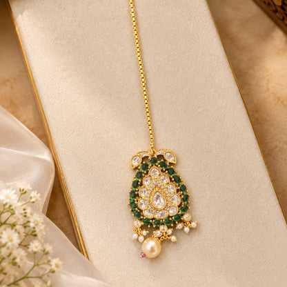 Gold-plated kundan polki paisley maang tikka with emerald green stone border, clear pear centre stone, cream pearl drop and box chain with hook