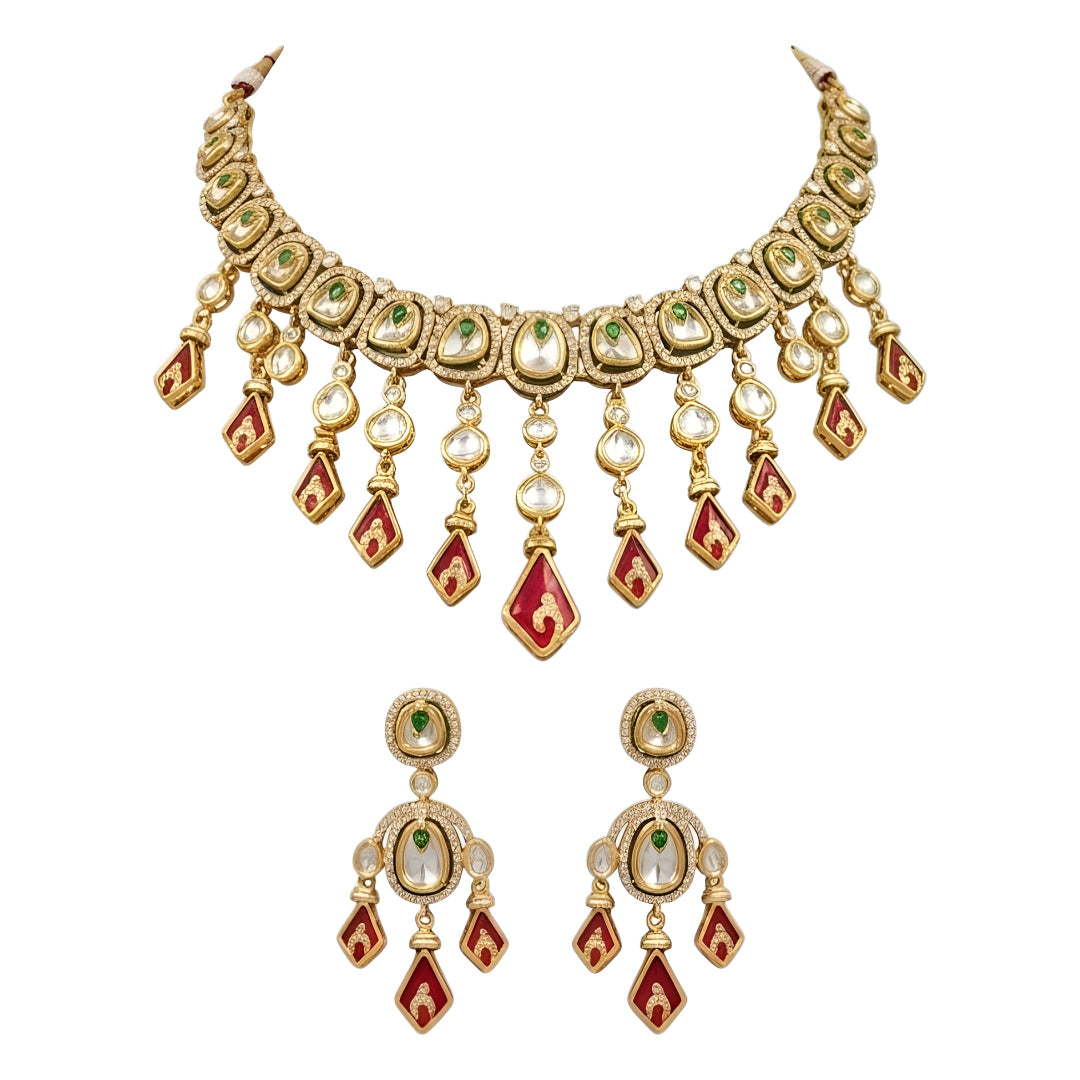 Gold-tone kundan necklace set with red kite-shaped drops, green accent stones and matching chandelier earrings on a grey display bust