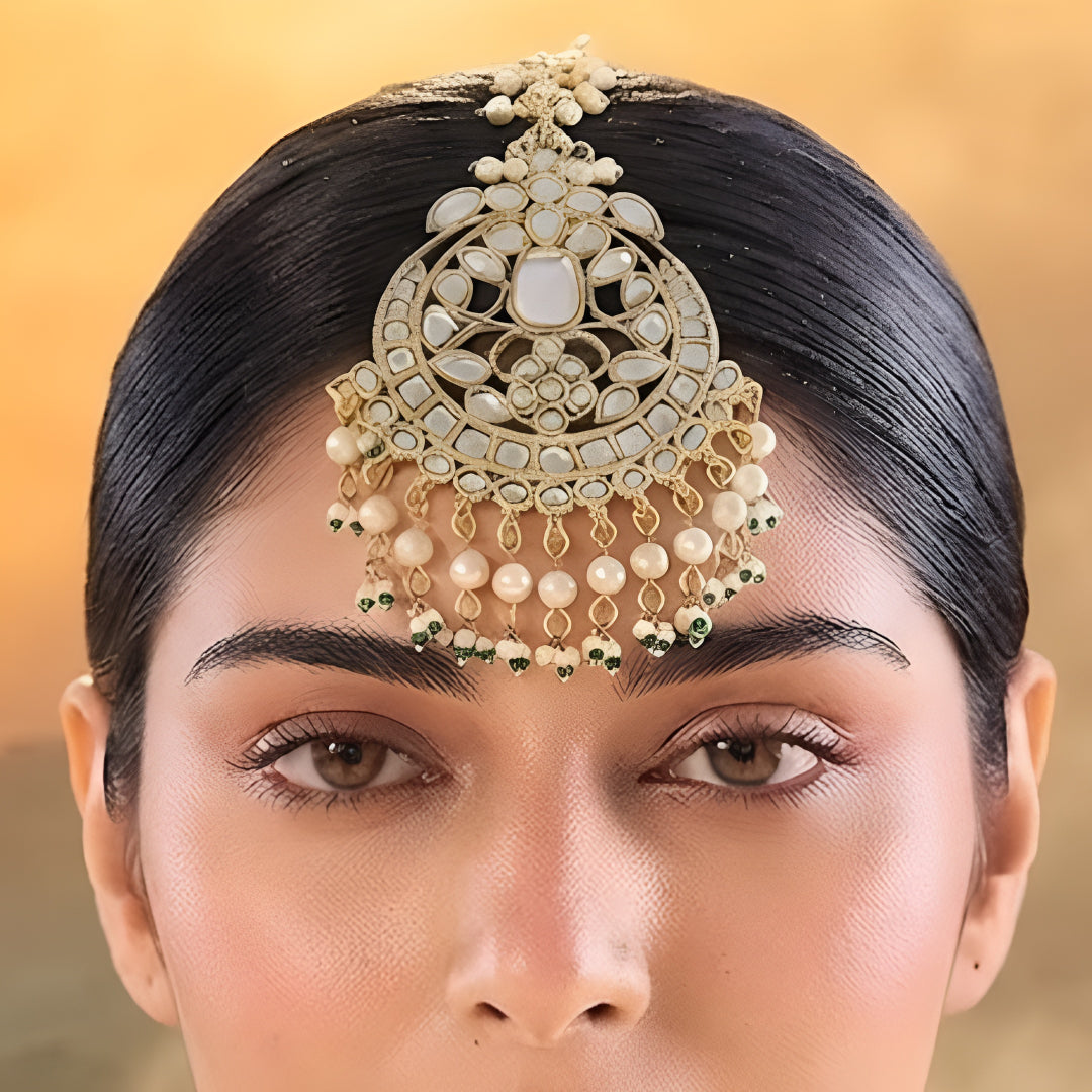 Gold kundan maang tikka with pearl and green bead tassels, traditional Indian bridal hair jewelry on white background