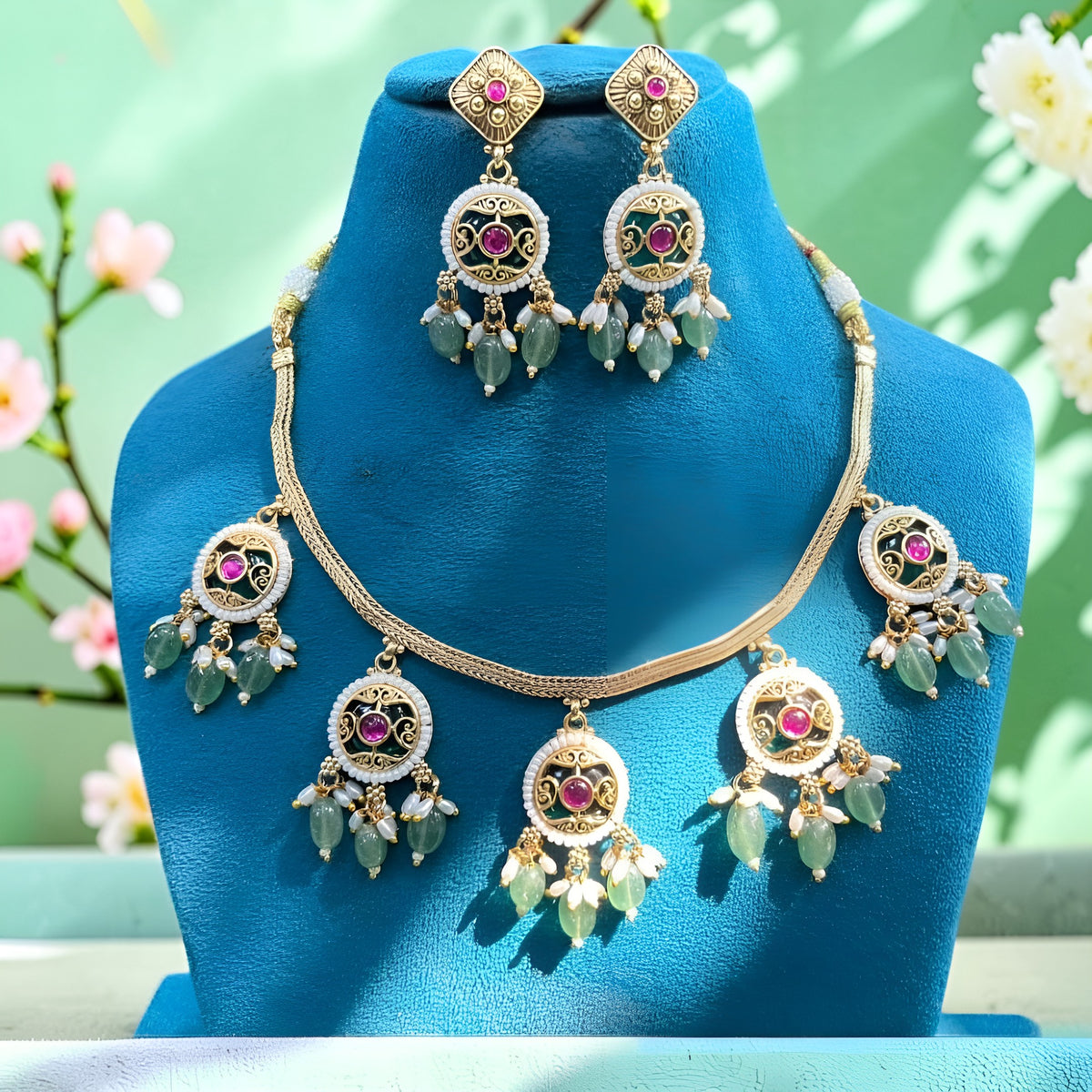 Antique gold plated choker necklace set with ruby pink medallions, mint green bead and pearl drops and matching earrings on a blue bust