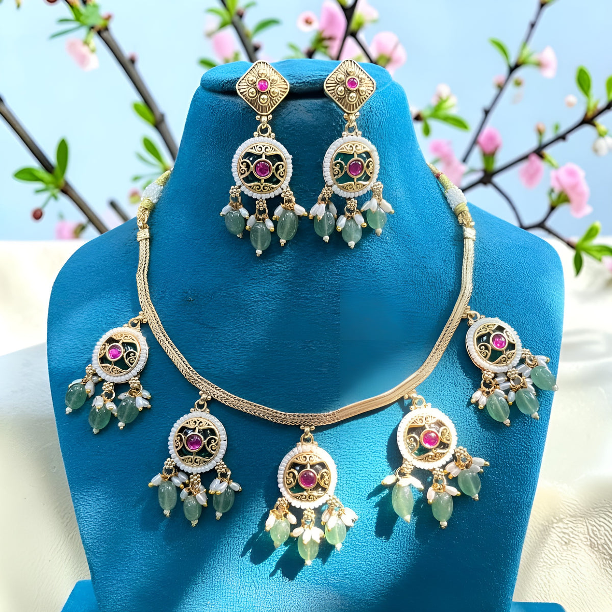 Antique gold plated necklace set with round ruby pink medallions, pastel green bead and pearl drops and matching earrings on a blue bust