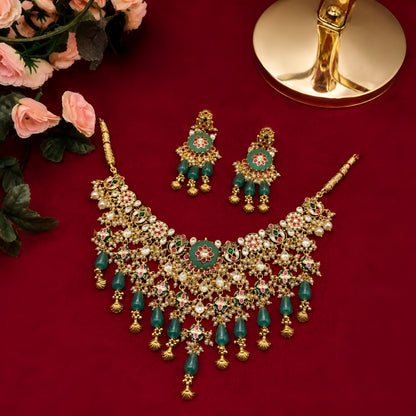 "Antique gold Kundan choker necklace and earring set with green floral meenakari centerpiece and emerald bead drops, traditional jewellery on maroon backdrop"