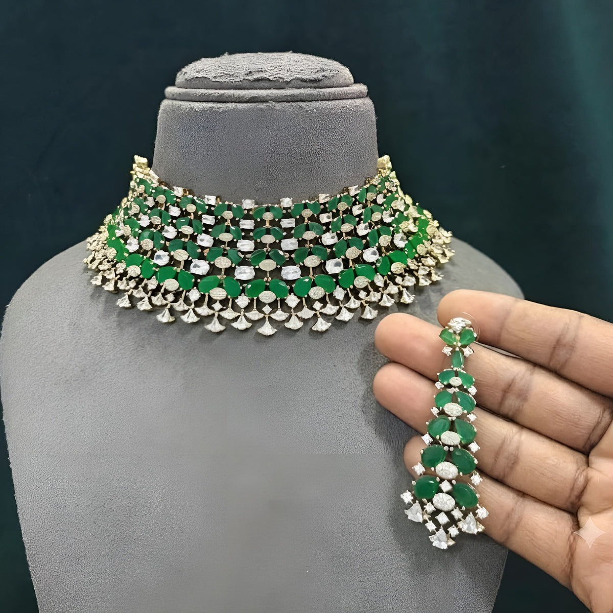 Emerald green American diamond choker necklace on a display bust with a matching long drop earring in hand