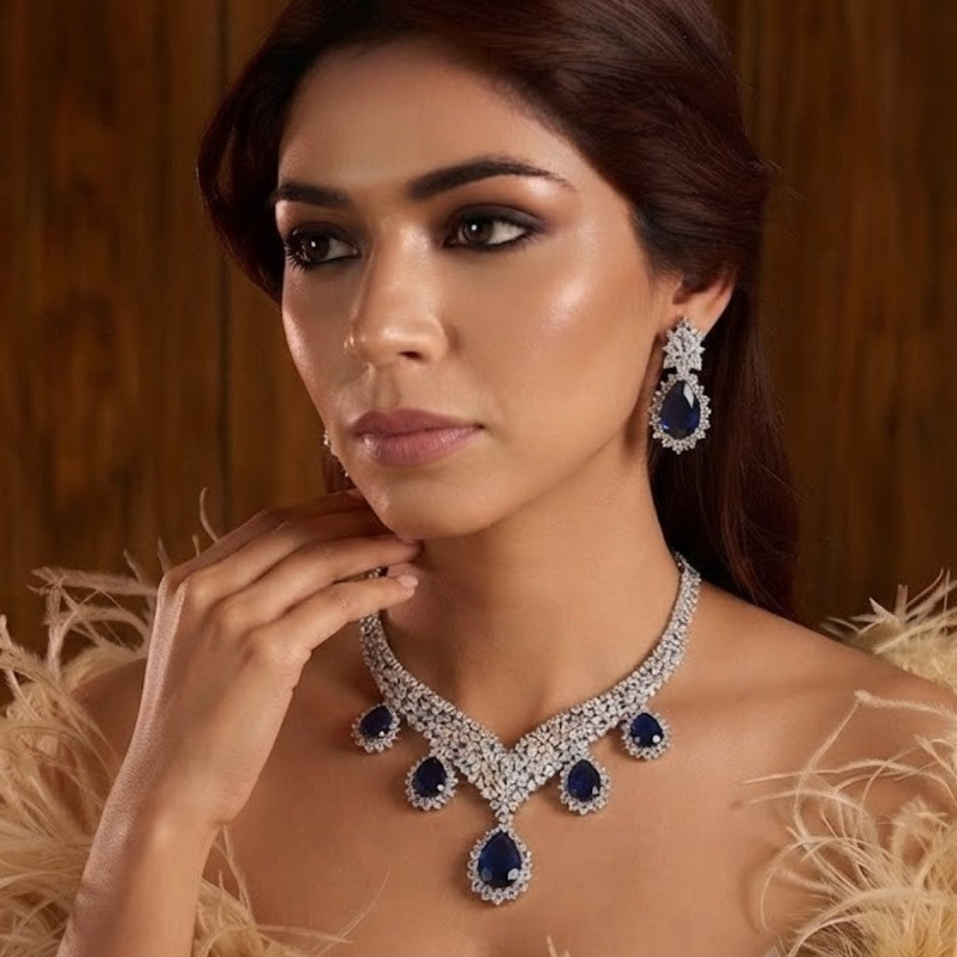 "Silver rhodium-plated V-shaped necklace set with white American diamonds and blue sapphire pear-drop stones, paired with matching teardrop earrings"