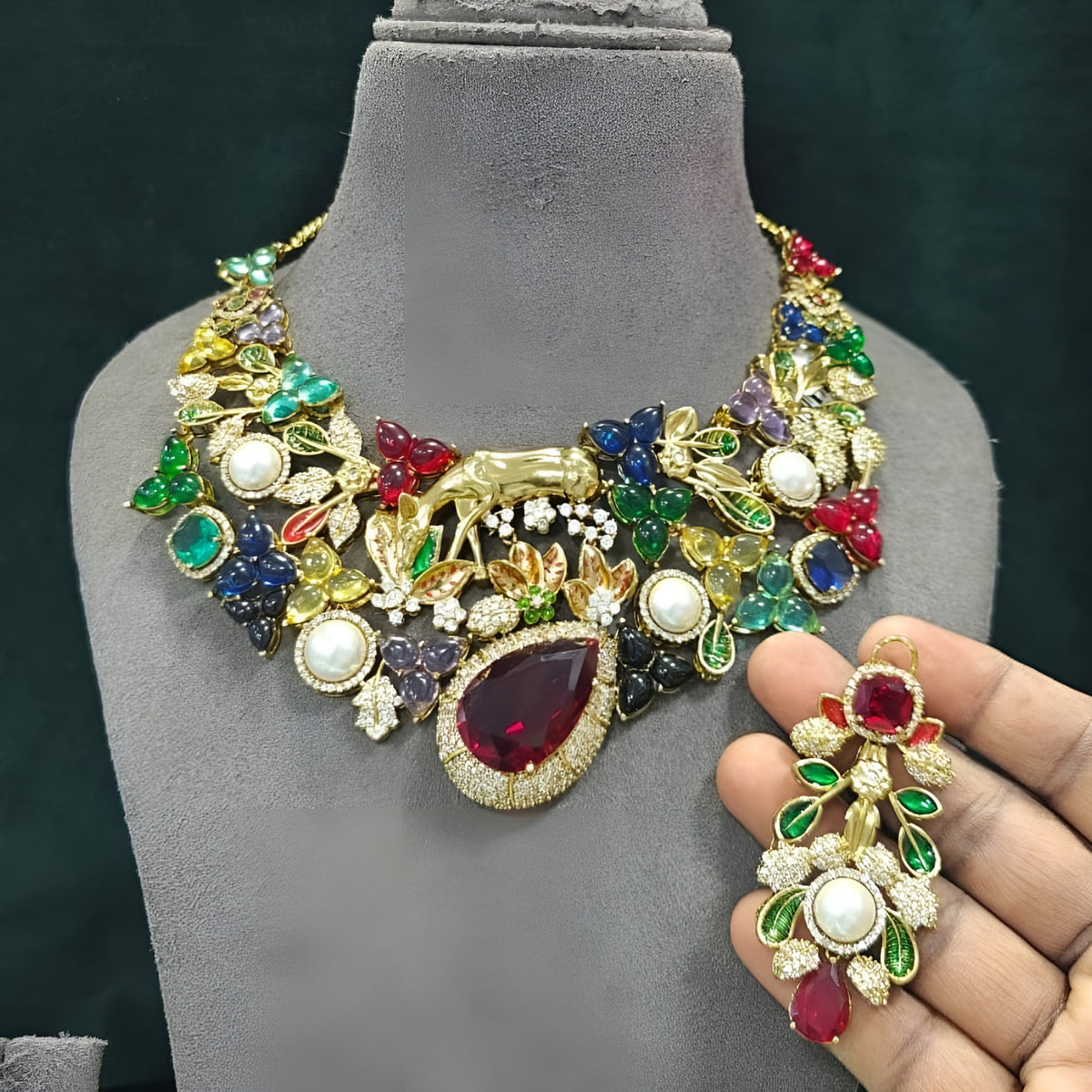 Gold plated multicolour designer necklace with ruby red teardrop centre stone, pearls and deer figure on a display bust
