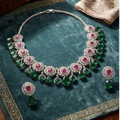 Luxury emerald green and ruby stone diamond-finish necklace set with matching earrings on white background.