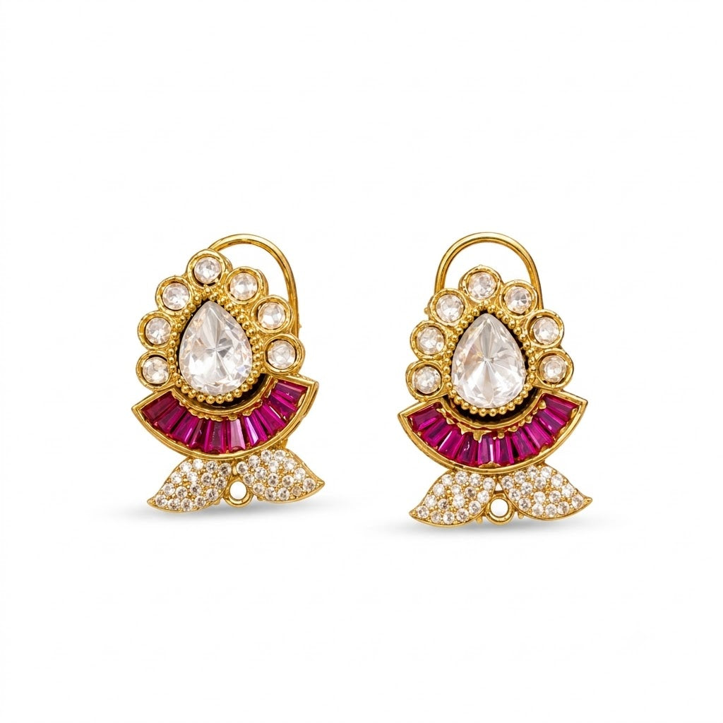 Pair of gold kundan-style stud earrings with a clear pear centre stone, ruby-pink baguette fan and zircon leaf base on a marble slab