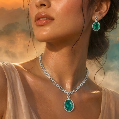 Silver-toned necklace set featuring an emerald green oval crystal pendant with matching drop earrings on a white background.