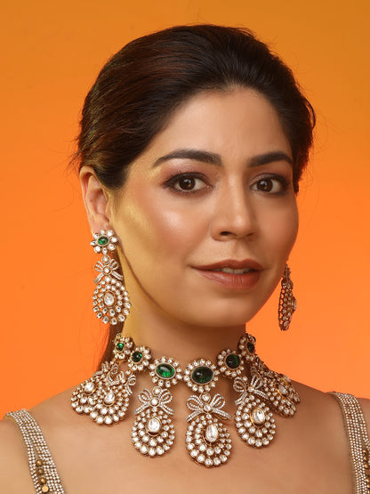 Gold-toned necklace with a braided cord and adjustable tassel tie, featuring intricate white stone detailing with oval green gemstones and multiple dangling teardrop motifs, paired with matching drop earrings, displayed on a plain light background.
