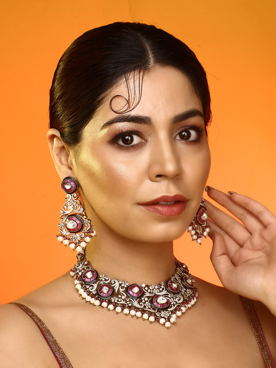 Gold-tone traditional necklace set with pink kundan-style stones, intricate detailing, pearl bead drops, and matching ornate dangling earrings.