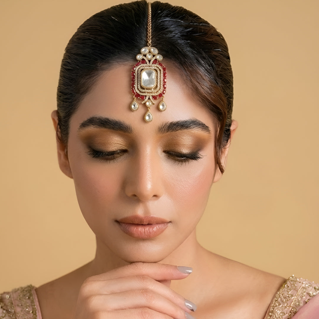 Gold-plated Kundan Maang Tikka featuring a rectangular white crystal centerpiece, ruby red stones, and elegant teardrop danglers for bridal and festive wear.