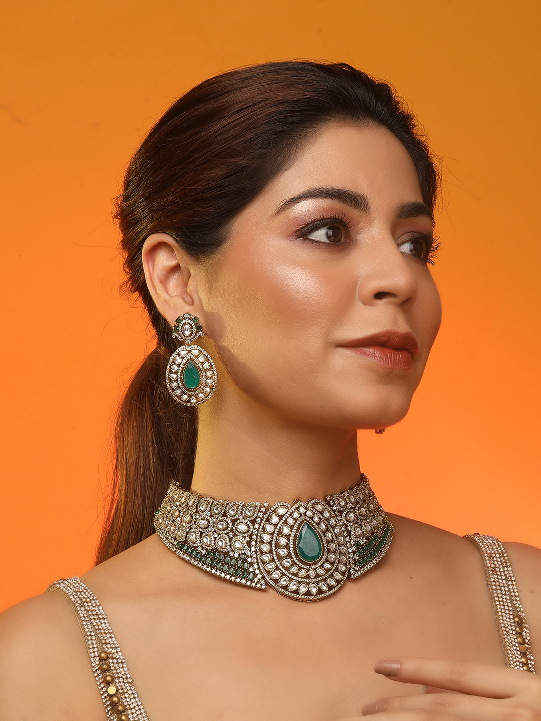 Gold-tone choker necklace set with intricate kundan-style detailing, highlighted by a large teardrop green stone centerpiece and matching drop earrings.