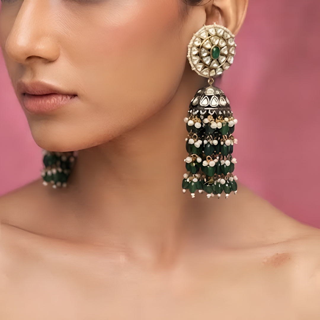 Green Kundan jhumka earrings with gold plating, emerald green center stone, pearl accents, and layered green bead tassels for bridal and festive wear.