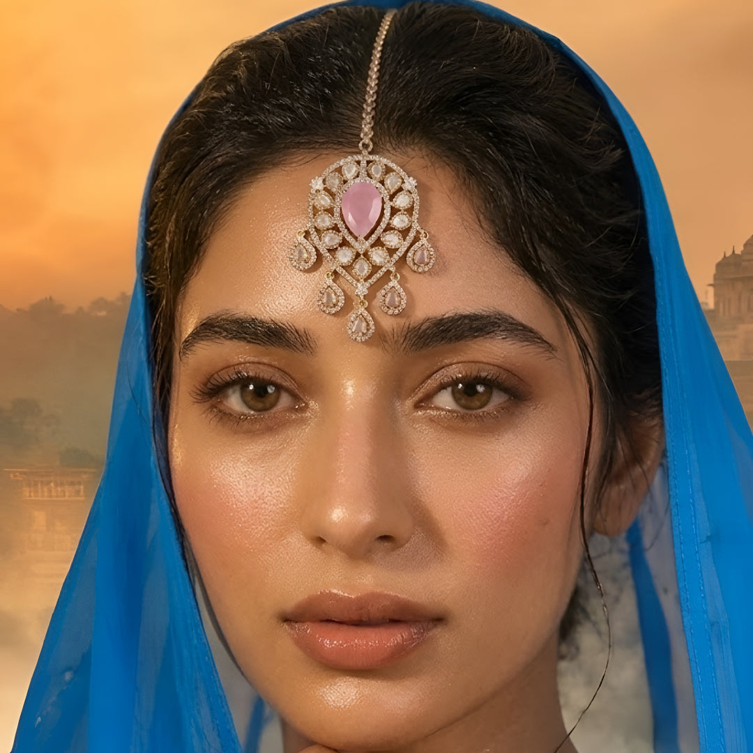Gold-plated bridal maang tikka with pink pear-shaped stone, Kundan-style teardrop crystals, and elegant dangling accents for weddings and festive wear.