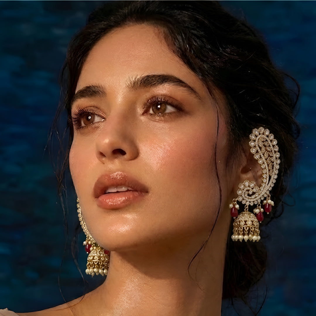 Luxury gold-plated Kundan Polki ear cuff jhumka earrings with ruby red bead drops, pearl tassels, and intricate floral detailing for bridal and festive wear.