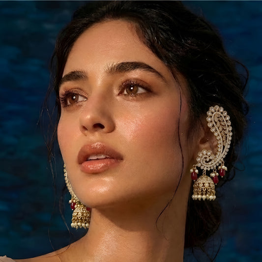 Luxury gold-plated Kundan Polki ear cuff jhumka earrings with ruby red bead drops, pearl tassels, and intricate floral detailing for bridal and festive wear.