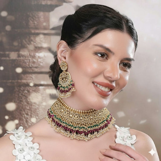 "Traditional gold-tone kundan bridal necklace set with ruby red and emerald green beads, paired with matching chandbali earrings on maroon silk background"