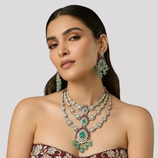 "Triple-layer gold-finish necklace set with green stones, purple detailing, American Diamond accents, pastel green bead drops, and matching earrings displayed on a light background."