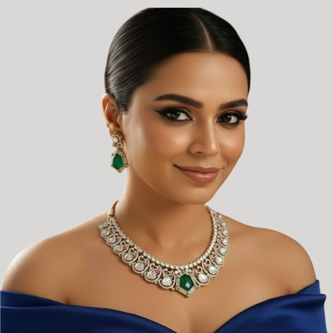 "Gold-finish necklace set with emerald green stones, white American Diamond detailing, red accents, and matching drop earrings displayed on a light background."