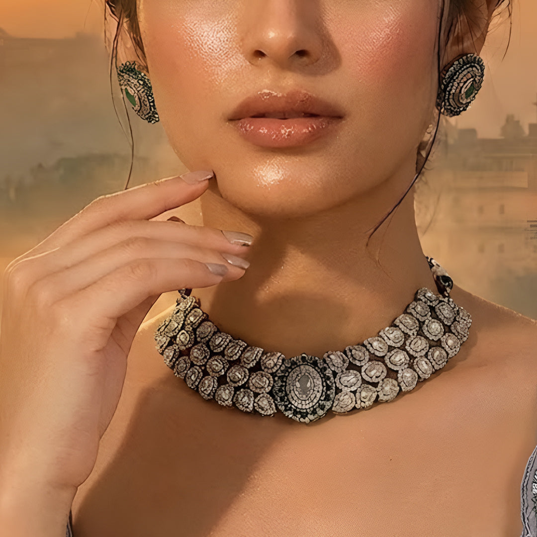 Elegant diamond and emerald choker necklace set with matching stud earrings featuring intricate floral motifs, sparkling white stones, green gemstone accents, and a luxurious gold-tone finish.