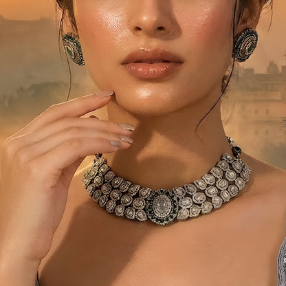 Elegant diamond and emerald choker necklace set with matching stud earrings featuring intricate floral motifs, sparkling white stones, green gemstone accents, and a luxurious gold-tone finish.