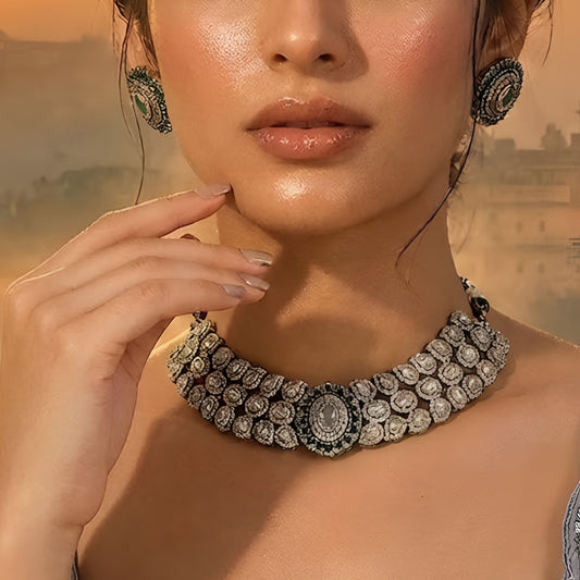 Elegant diamond and emerald choker necklace set with matching stud earrings featuring intricate floral motifs, sparkling white stones, green gemstone accents, and a luxurious gold-tone finish.