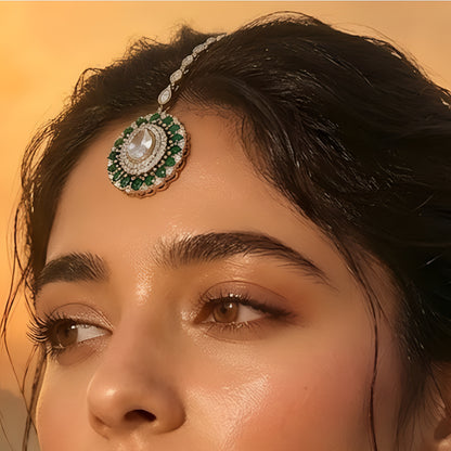 Gold-plated green American diamond bridal maang tikka with oval crystal centerpiece and green marquise stones on a white background.