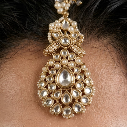 Gold-plated Kundan maang tikka with sparkling clear stones, pearl bead drops, and an elegant bridal design for weddings and festive wear.