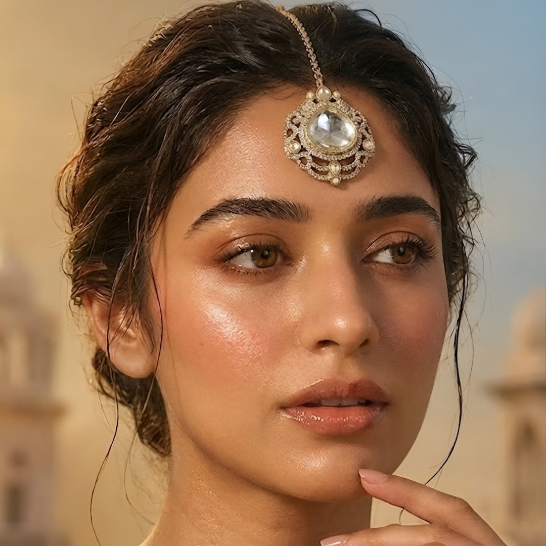 Elegant gold-tone crystal bridal maang tikka with intricate filigree design and large clear stone centerpiece for weddings and festive wear.