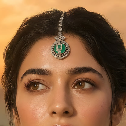 Gold-plated American Diamond maang tikka with an emerald-green center stone and circular pendant for bridal and festive wear.