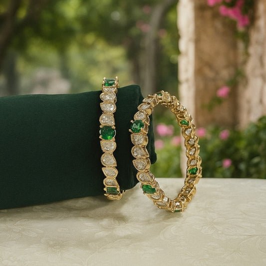Set of gold-plated bangles with tear-drop shaped white Kundan stones and green accents displayed on a green velvet roll.