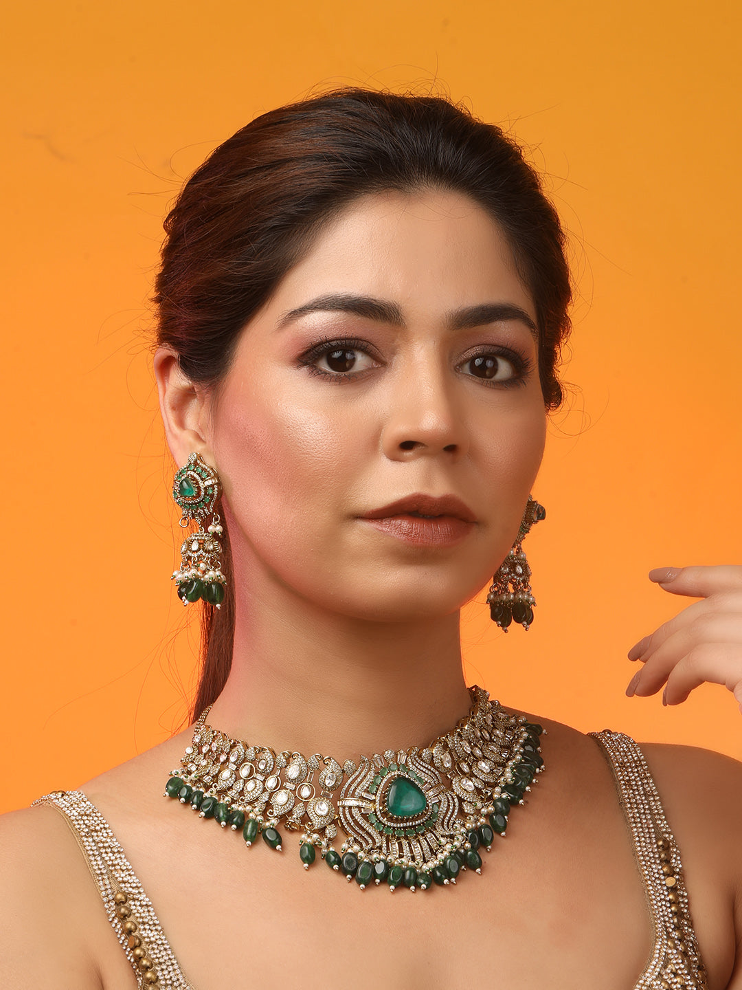 Detailed gold-toned statement necklace with intricate white stone embellishments and a prominent green teardrop centerpiece, finished with dangling green beads and pearls, paired with matching ornate drop earrings, displayed on a plain light background.