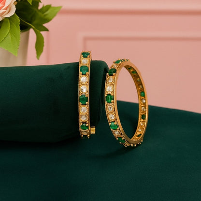 Set of gold-plated bangles adorned with alternating green and white Kundan stones, displayed on a dark green velvet roll against a white background.
