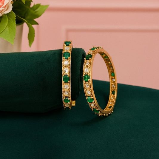 Set of gold-plated bangles adorned with alternating green and white Kundan stones, displayed on a dark green velvet roll against a white background.