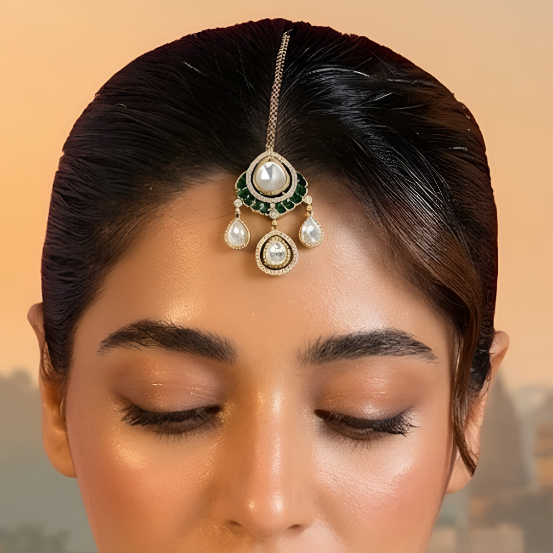 Gold-toned Kundan teardrop maang tikka with green stone detailing and three dangling teardrop charms for bridal and festive wear.