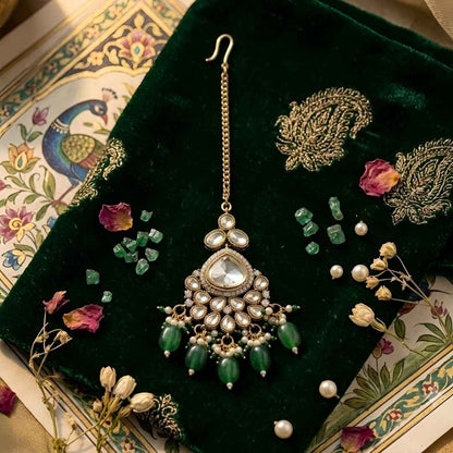 Gold plated Kundan maang tikka with white Polki stones, green bead drops, and pearl detailing for bridal wedding and festive wear.