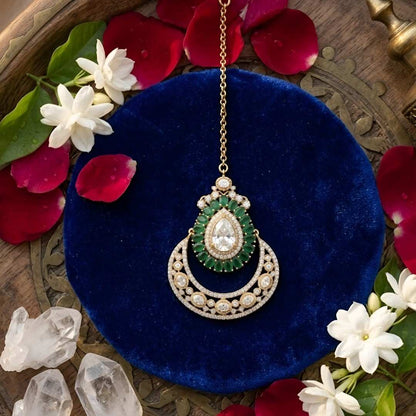 Elegant gold-plated bridal maang tikka featuring a pear-shaped crystal, green stones, and crescent crystal design for weddings and festive occasions.